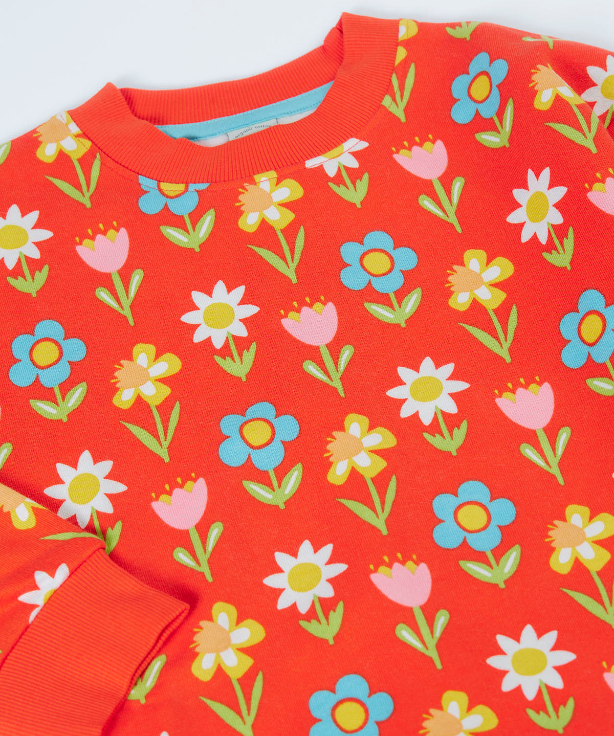 A close up of the Frugi organic cotton sweatshirt laid flat. In red with a repeating flower print