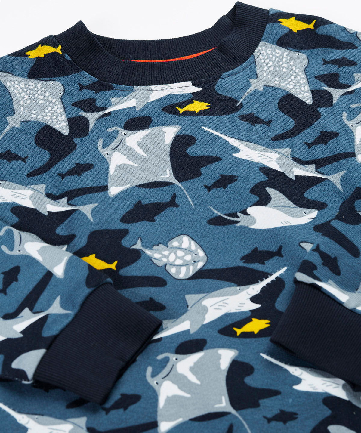 A close up of the Frugi organic cotton sweatshirt laid flat. In dark blue and navy trim with a repeating grey manta ray and shark print.