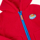 Close up of the front of the Frugi red fleece hooded children's jacket with contrasting blue zip trim and guard and orange zip pull. Badge detail featuring the words happy days and an image of the sun on the chest. Two front pockets with navy binding. 