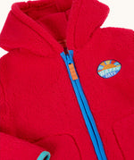 Close up of the front of the Frugi red fleece hooded children's jacket with contrasting blue zip trim and guard and orange zip pull. Badge detail featuring the words happy days and an image of the sun on the chest. Two front pockets with navy binding. 