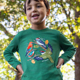 A child standing outside by trees and wearing the Frugi kids terrific applique top in holly green/birds. A dark green long sleeved GOTS organic top with different bird appliques