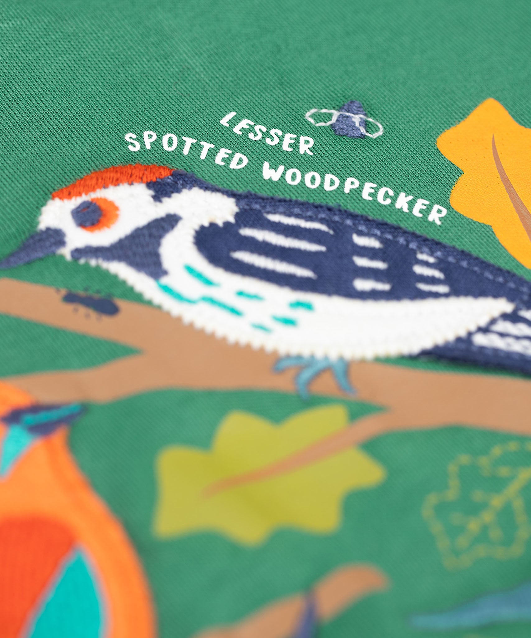 A close up of the Frugi kids terrific applique top in holly green/birds showing the woodpecker applique detail on dark green organic cotton fabric.
