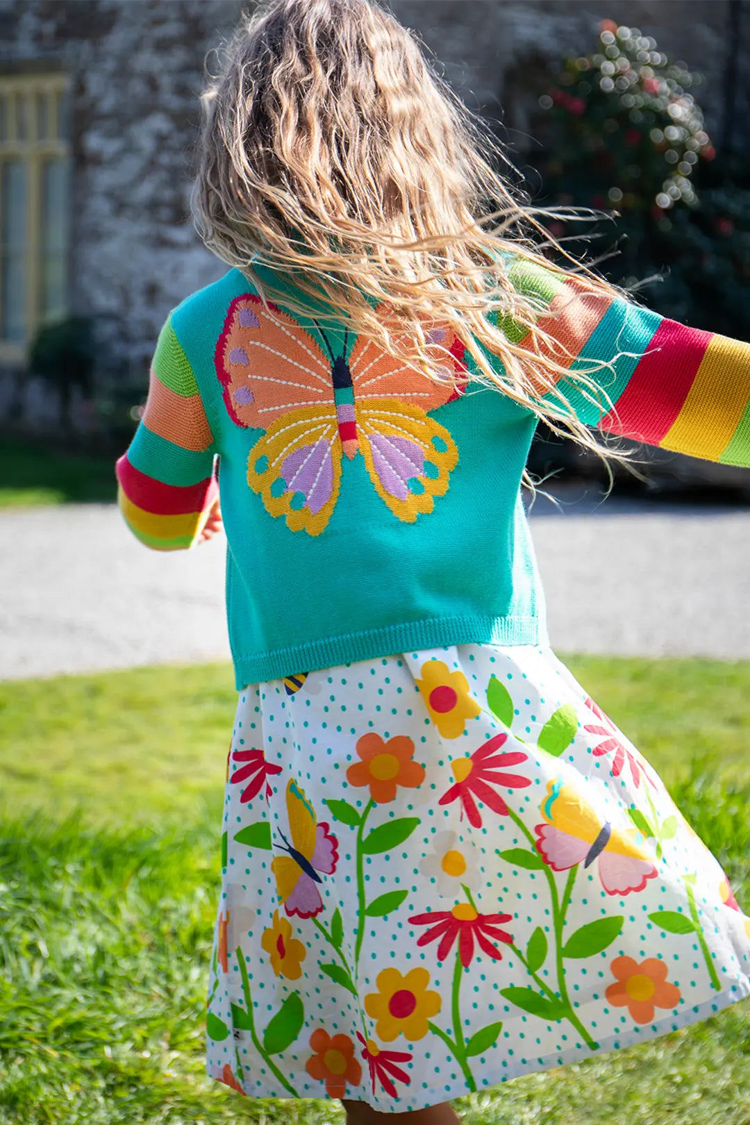 Child wearing a Frugi Organic colorful dress with butterfly and floral patterns outdoors. to represent the Summer Sale at Babipur. 