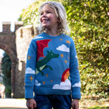 A child wearing the Frugi elwood dragon skies knitted jumper. A GOTS organic cotton jumper in light blue with a playful flying dragon design wrapping around the jumper. Features button fasteners on the shoulder. This children's knitted jumper is apart of a wide range of organic cotton clothing for children available here at Babipur. 