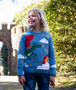 A child wearing the Frugi elwood dragon skies knitted jumper. A GOTS organic cotton jumper in light blue with a playful flying dragon design wrapping around the jumper. Features button fasteners on the shoulder. This children's knitted jumper is apart of a wide range of organic cotton clothing for children available here at Babipur. 