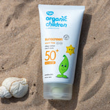 Green People organic children SPF50 scent free sun cream lying flat on sand next to a shell