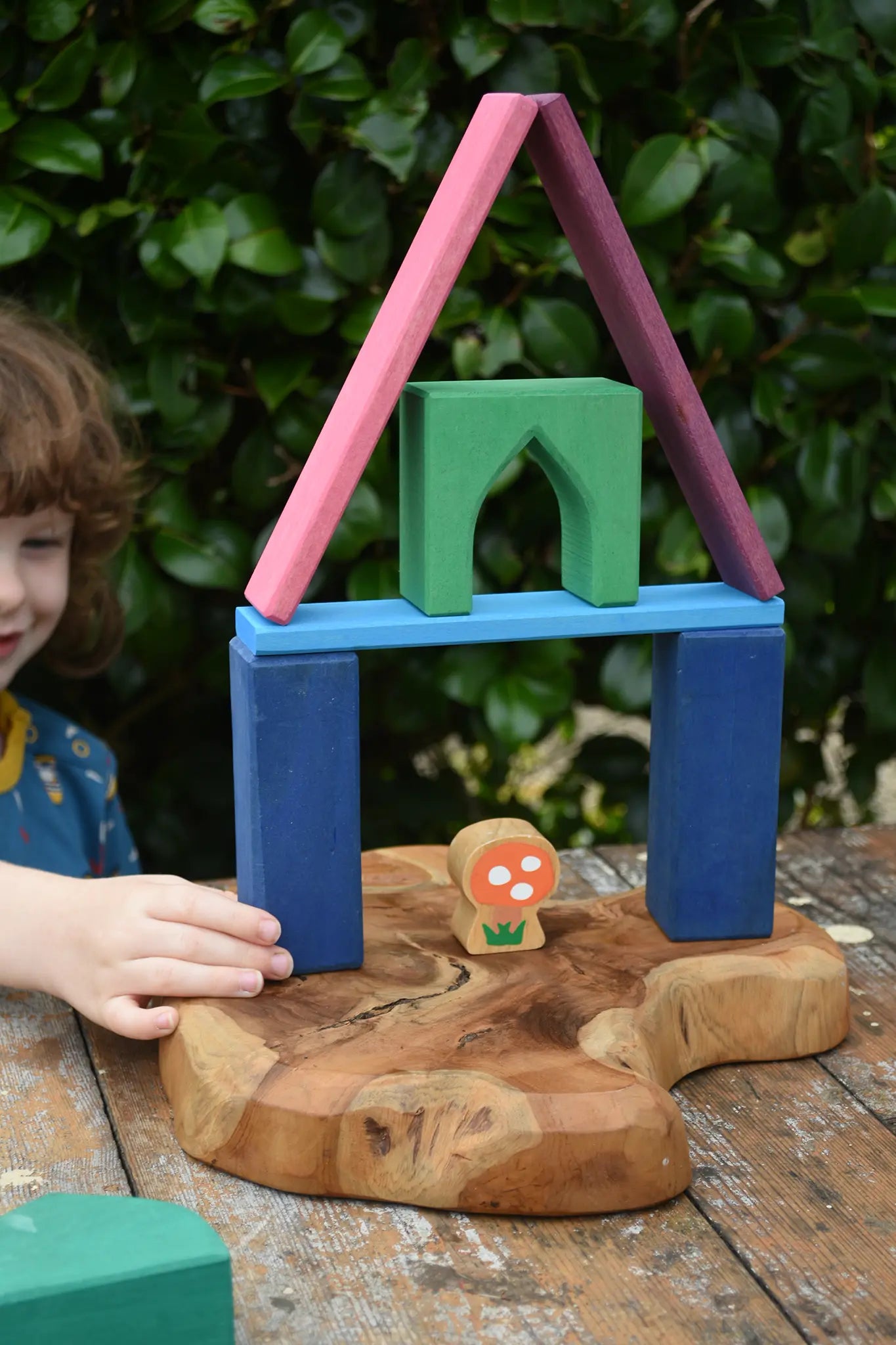 Child playing with the Glückskäfer building block set stacking pieces with Grimm's 1001 nights blocks with a Lanka Kade Babipur mushroom placed underneath.