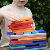 Child stacking Glückskäfer colorful wooden rectangular blocks on a carved wooden board outdoors.