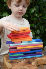 Child stacking Glückskäfer colorful wooden rectangular blocks on a carved wooden board outdoors.