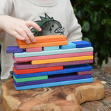 Child stacking Glückskäfer colorful wooden rectangular blocks on a carved wooden board outdoors.