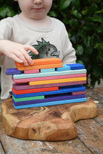 Child stacking Glückskäfer colorful wooden rectangular blocks on a carved wooden board outdoors.