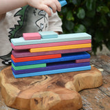 Child stacking slats from the Glückskäfer building slat set on a wooden surface.
