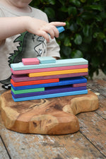 Child stacking slats from the Glückskäfer building slat set on a wooden surface.