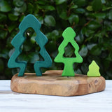 Three pieces from the Glückskäfer 6-Piece Fir Tree wooden tree stacking toy placed on a wooden surface outdoors. Large, medium and small size next to each other.