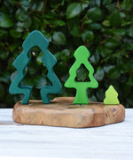 Three pieces from the Glückskäfer 6-Piece Fir Tree wooden tree stacking toy placed on a wooden surface outdoors. Large, medium and small size next to each other.