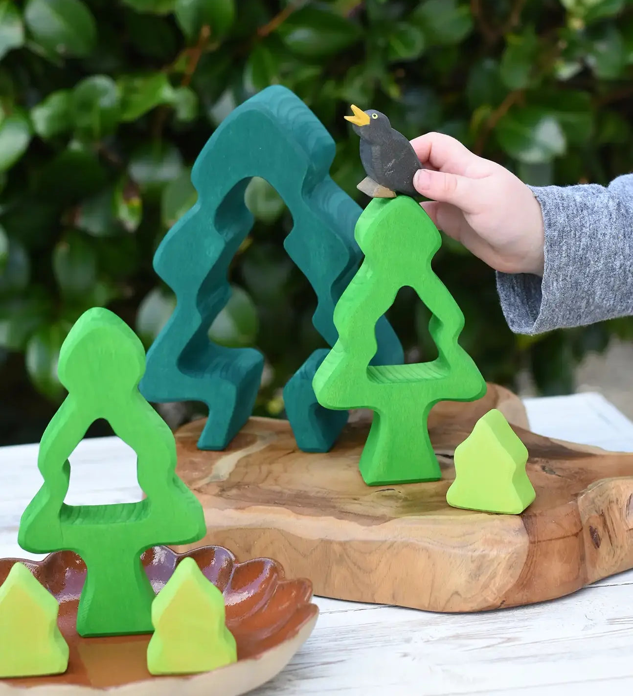 Child playing with the Glückskäfer 6-Piece Fir Tree wooden tree with the pieces placed on a wooden surface The child has an Ostheimer black bird in his hand. 