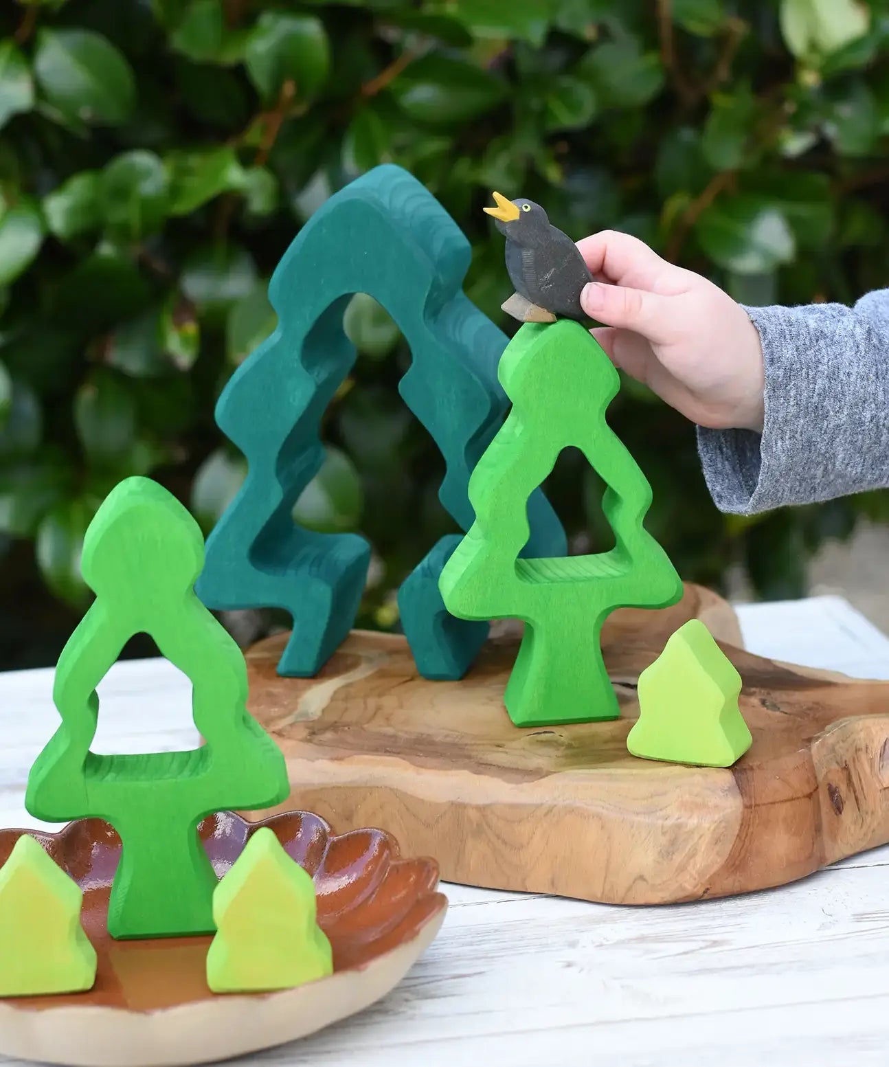 Child playing with the Glückskäfer 6-Piece Fir Tree wooden tree with the pieces placed on a wooden surface The child has an Ostheimer black bird in his hand. 
