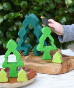 Child playing with the Glückskäfer 6-Piece Fir Tree wooden tree with the pieces placed on a wooden surface The child has an Ostheimer black bird in his hand. 