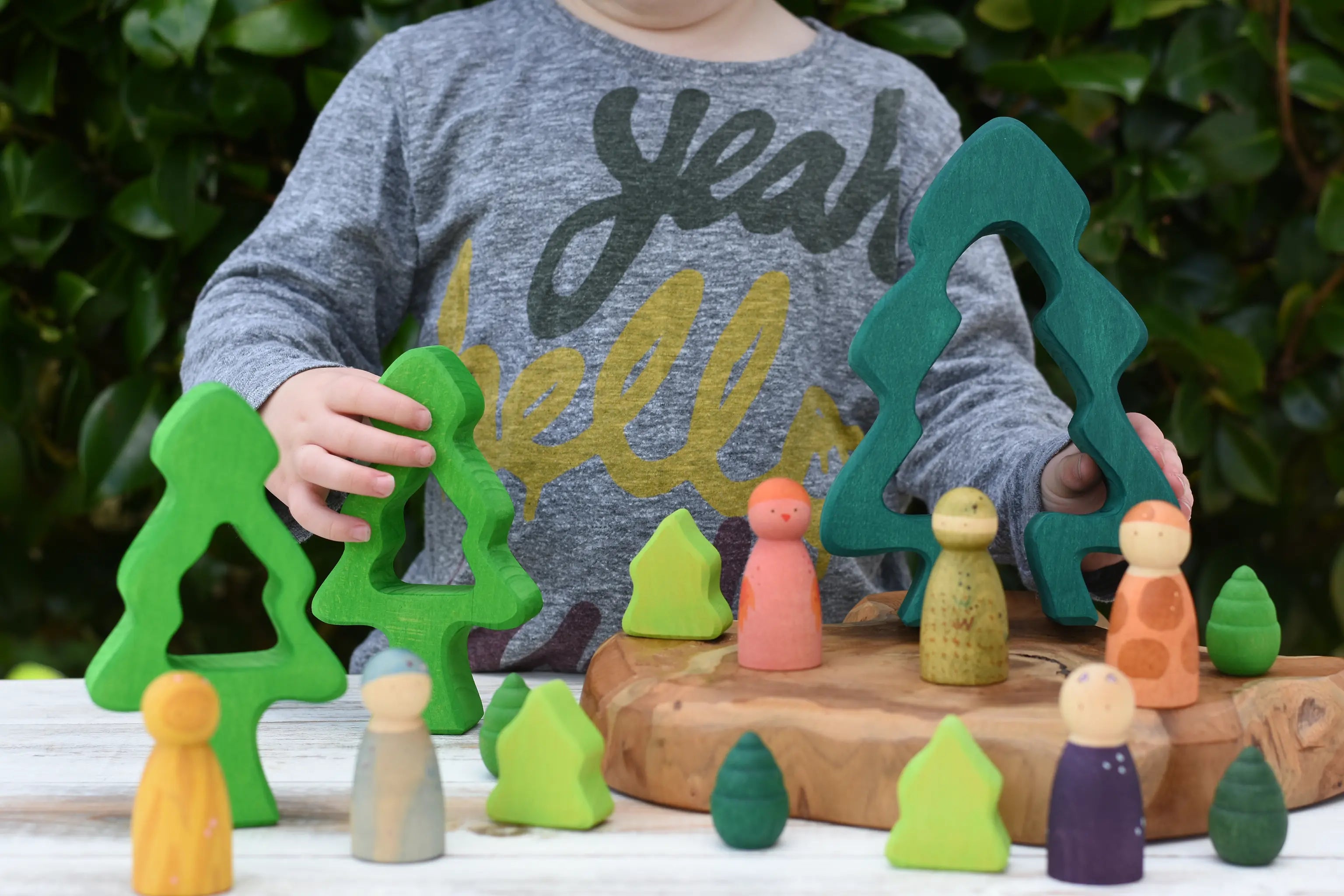 Child playing with the Glückskäfer 6-Piece Fir Tree wooden tree stacking toy in a small world play scene with Grapat wild crew animal nins. 
