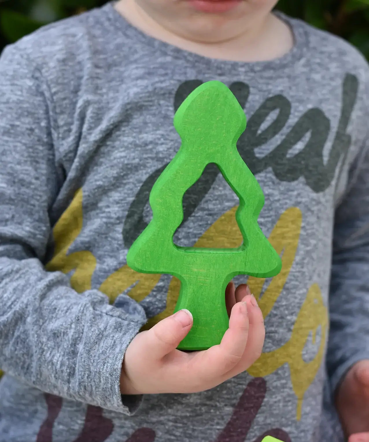 Child holding one of teh middle pieces from the Glückskäfer 6-Piece Fir Tree wooden tree stacking toy in his hans.