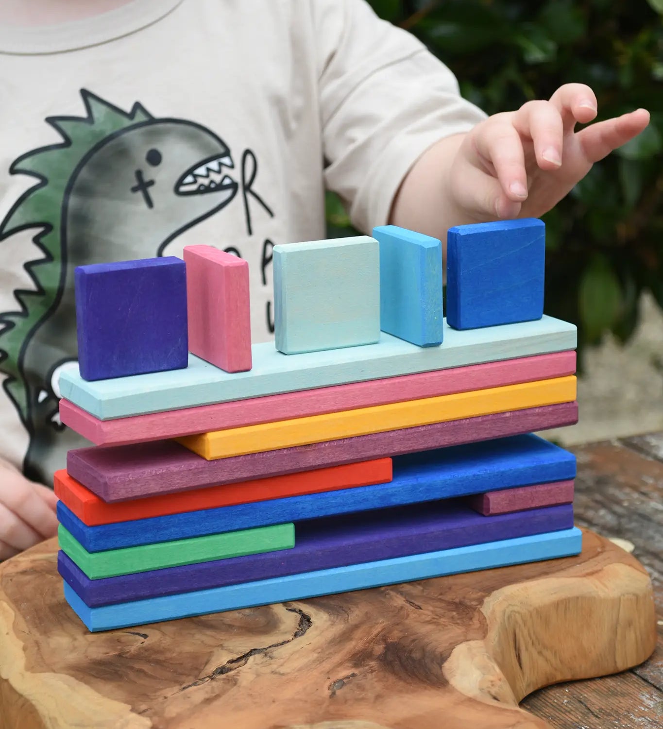 Child's hands stacking the colorful Glückskäfer building slats on a wooden surface outdoors.