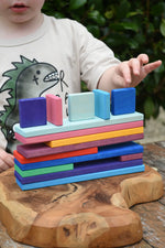 Child's hands stacking the colorful Glückskäfer building slats on a wooden surface outdoors.