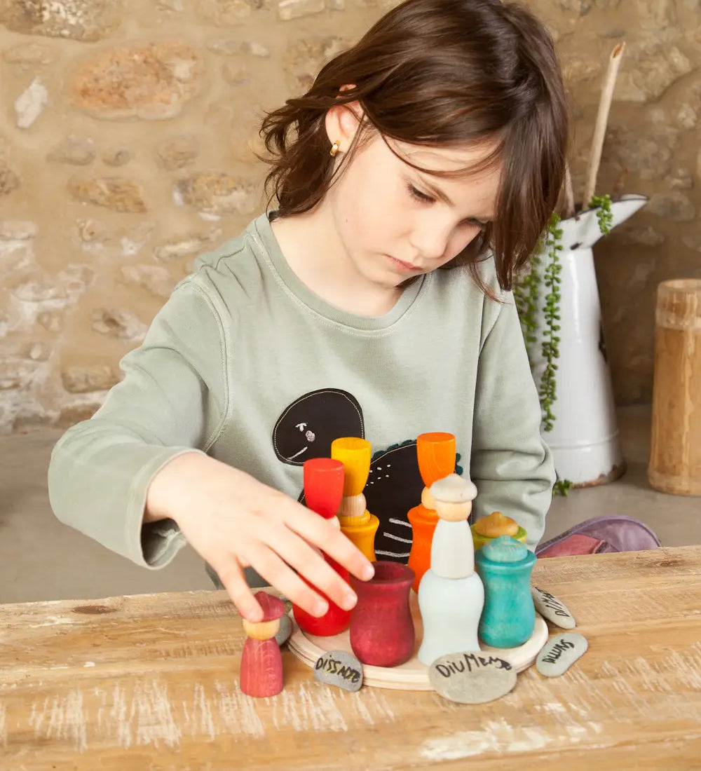 Child balancing coloured wooden peg dolls inside the matching cups from the Grapat handcrafted wooden 7 moons weekly calendar set