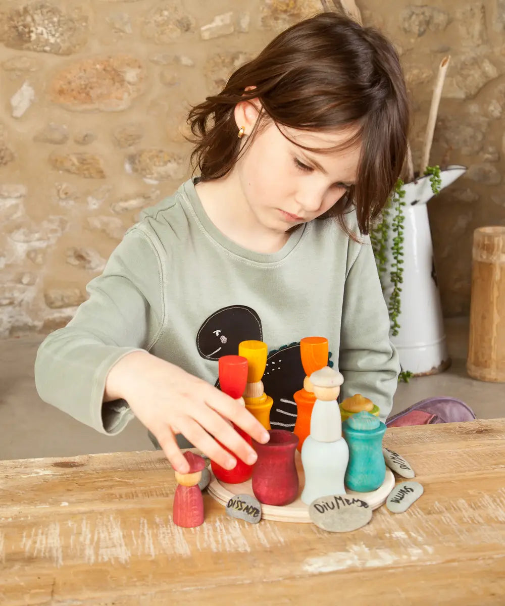 Child balancing coloured wooden peg dolls inside the matching cups from the Grapat handcrafted wooden 7 moons weekly calendar set
