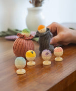 Six little wooden figures representing different fruits and vegetables. There is a green, orange, blue, yellow, purple and pink/red figure. With the green and orange figure inside a sock like a sock puppet