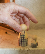 A closer look at the Nin wearing the painted apron, and another small wooden figure next to it. The small wooden figure is also light wood and is painted in light blue and purple on the bottom half.