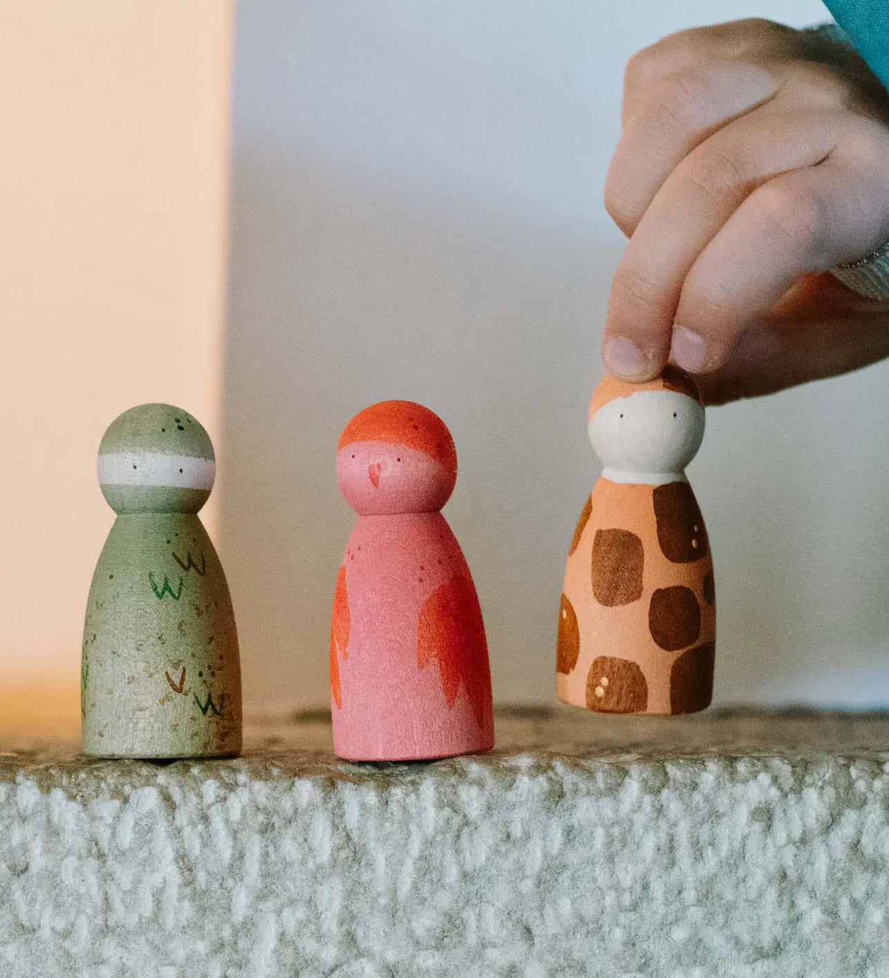 Child's hand holding Grapat Animal Crew - wooden nin peg dolls, hand painted as animals, bird, crocodile and leopard.