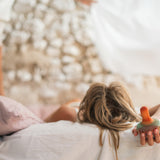 A child lying on a bed holding the Grapat wooden mellow orange wobbly bird in the hand