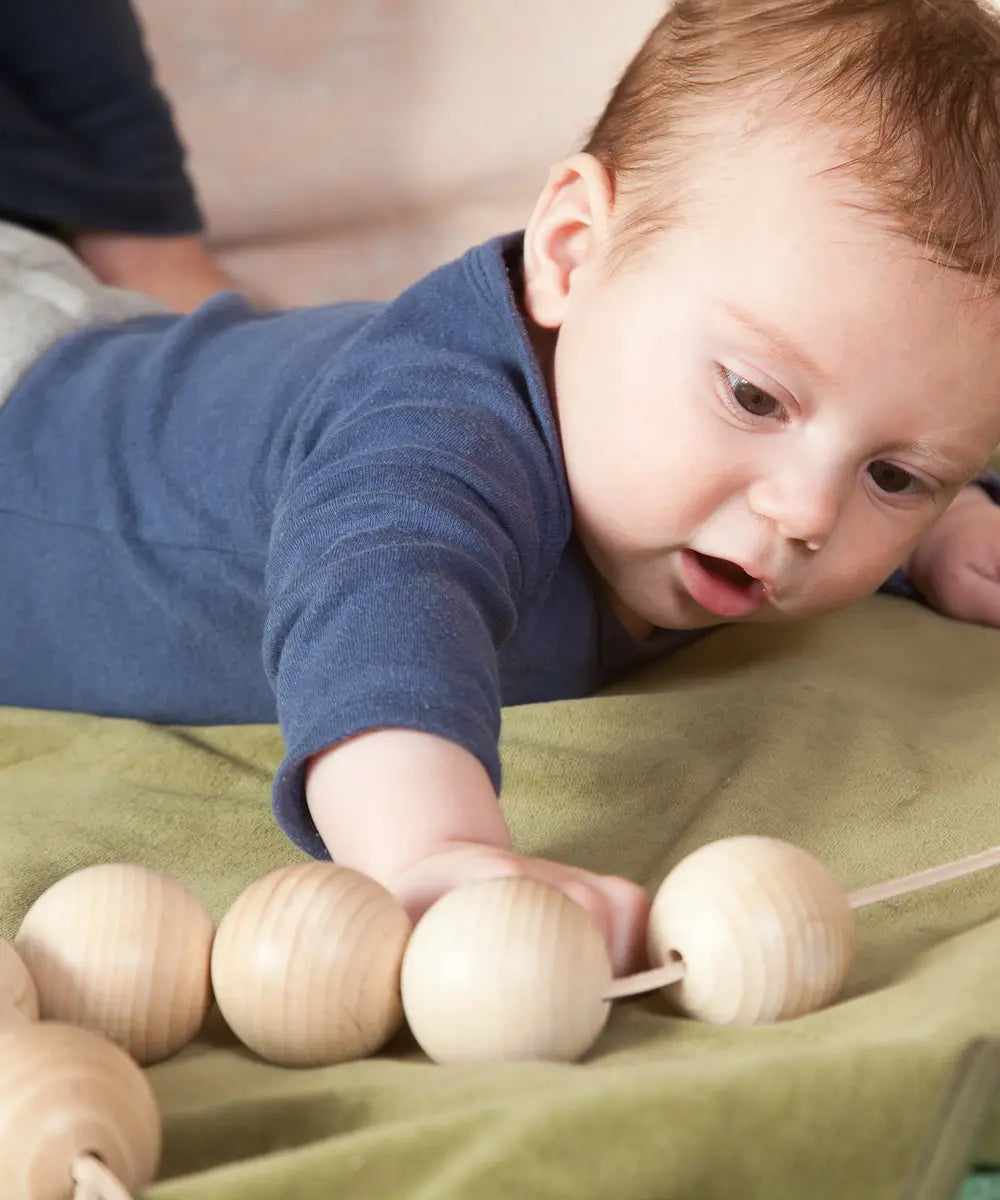 Baby reaching out for the Grapat natural wooden sensory ball garland on a green blanket
