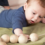Baby reaching out for the Grapat natural wooden sensory ball garland on a green blanket