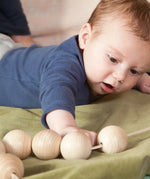 Baby reaching out for the Grapat natural wooden sensory ball garland on a green blanket