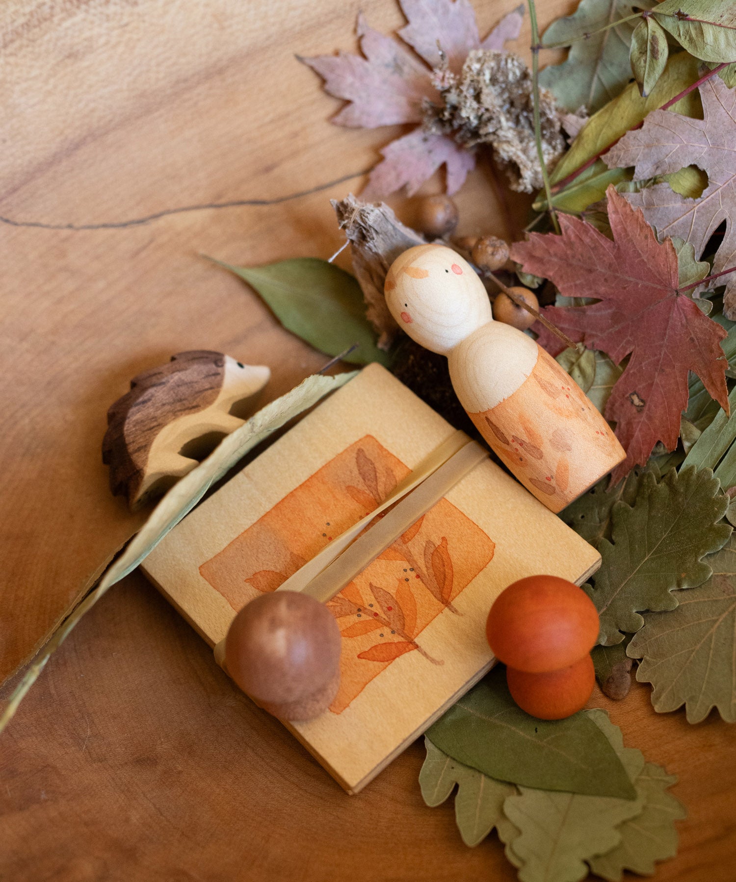 Grapat / Ostheimer hello Autumn wooden set available at Babipur. Handmade and hand painted wooden pieces set on a wooden surface with Autumn leaves