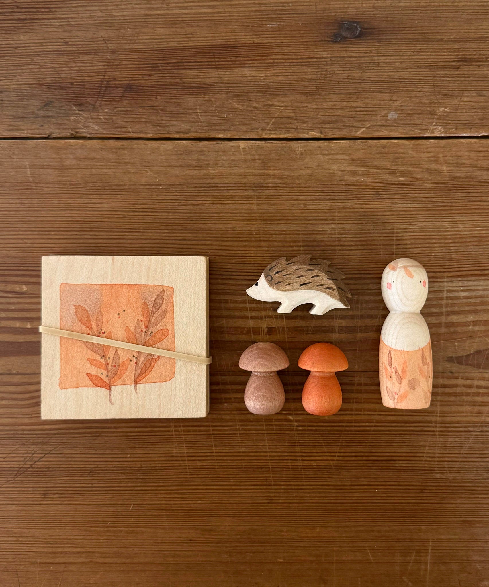 A top down image of the Grapat / Ostheimer hello Autumn wooden set available at Babipur. Each handmade and hand painted wooden piece is displayed on a wooden surface