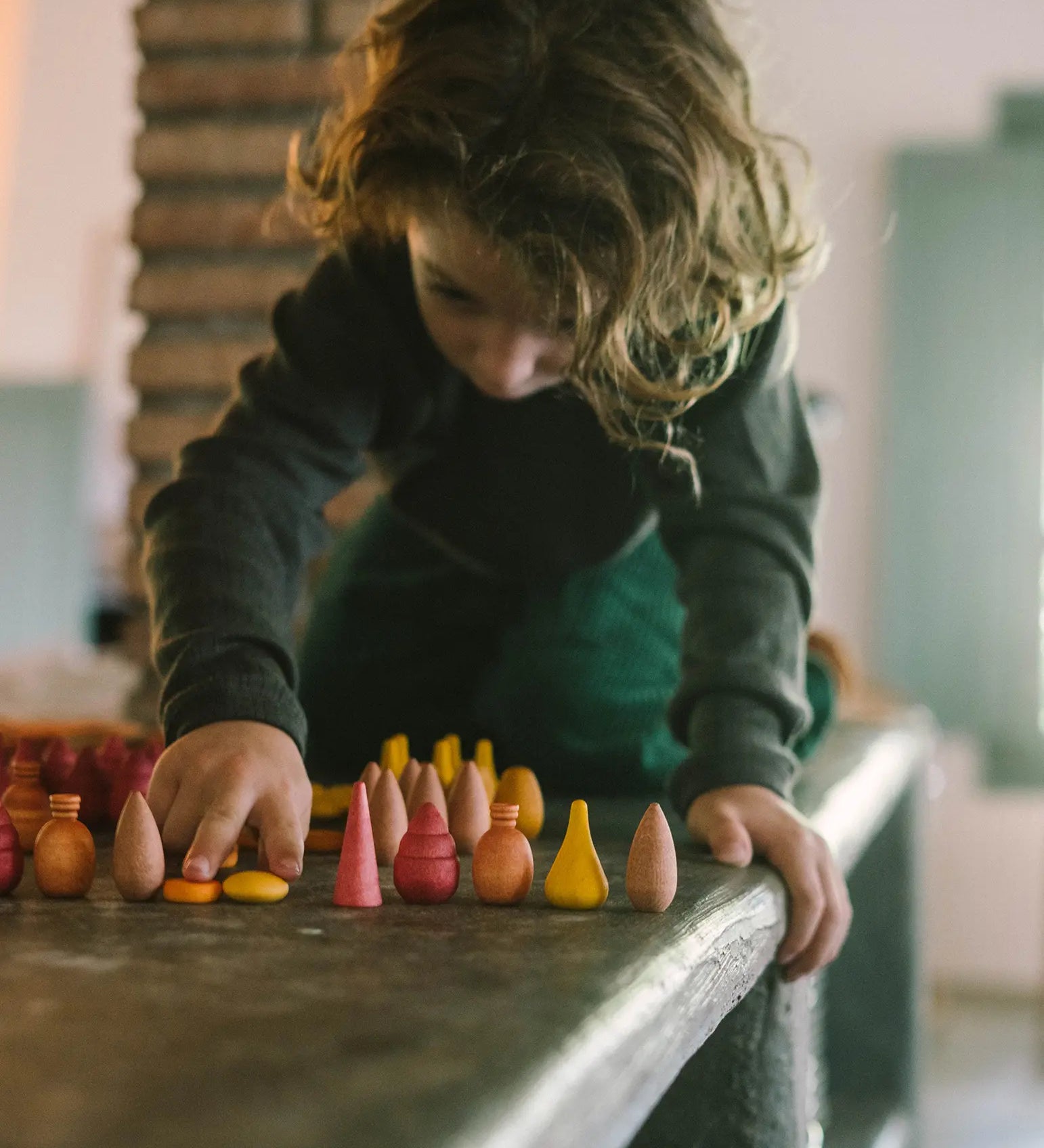Child sorting different Grapat handcrafted wooden mandala pieces on a table. Each piece is hand painted in warm colours