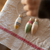 Grapat Handmade and handpainted Wooden winter sparkle decorations available at Babipur on a cloth with a child's hand above the decorations. 