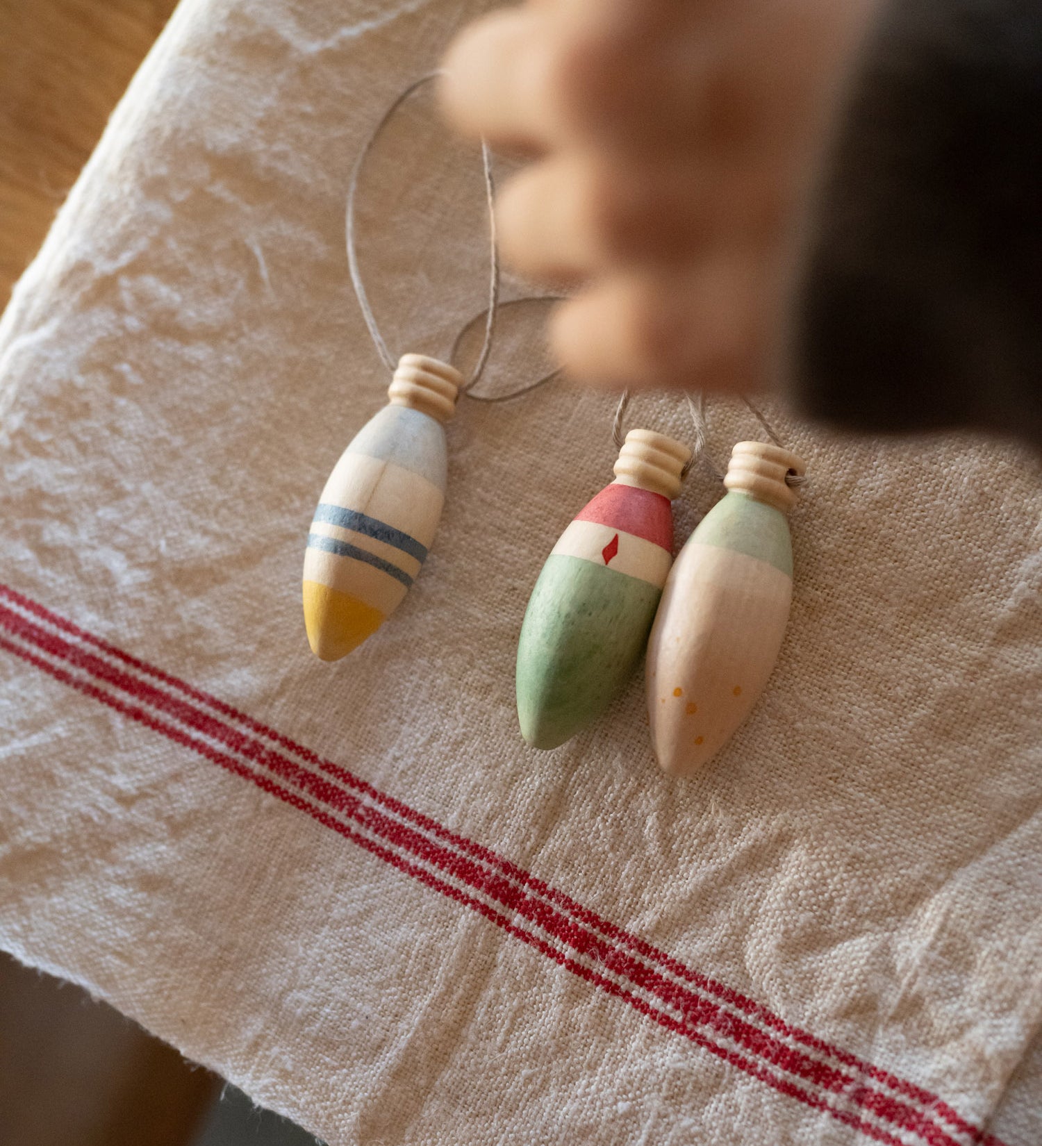Grapat Handmade and handpainted Wooden winter sparkle decorations available at Babipur on a cloth with a child's hand above the decorations. 