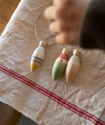 Grapat Handmade and handpainted Wooden winter sparkle decorations available at Babipur on a cloth with a child's hand above the decorations. 