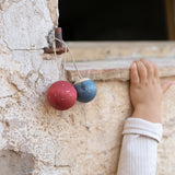 2 handmade and hand painted wooden Grapat wish balls hanging outside with a child's arm in the background