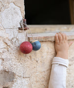 2 handmade and hand painted wooden Grapat wish balls hanging outside with a child's arm in the background