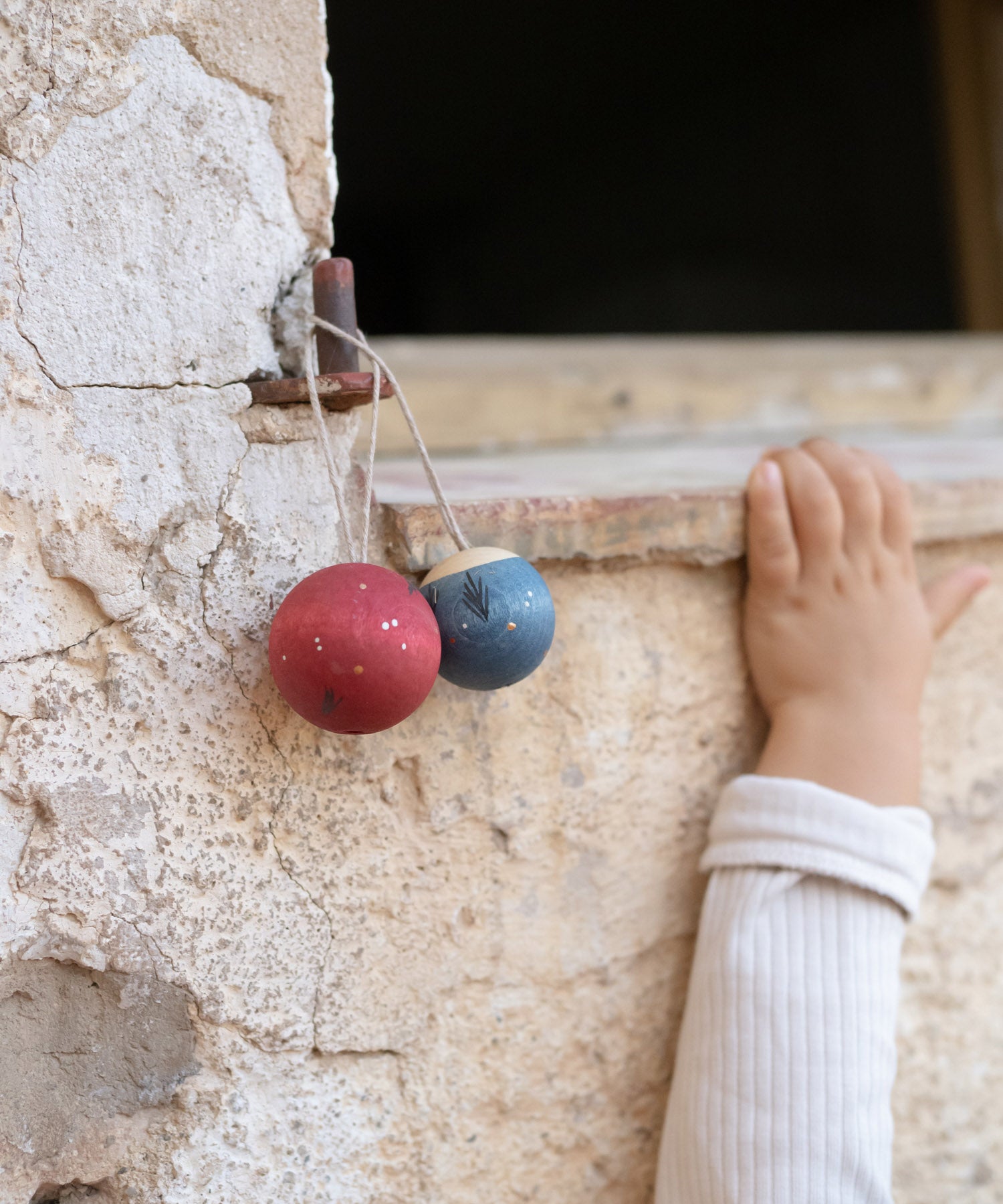 2 handmade and hand painted wooden Grapat wish balls hanging outside with a child's arm in the background