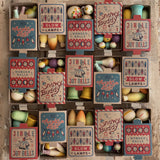 The Grapat Wooden Christmas Ornaments in their boxes, with the boxes lined up in three rows of 5. Each box has a whimsical Christmas design and the handmade and and painted ornaments can be used year after year.