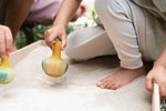 A close up of the Grapat wooden yellow flowing bird. Showing the handpainted face detail and feathers. Bird is held by a child in the Grapat wooden freeplay tray set filled with sand