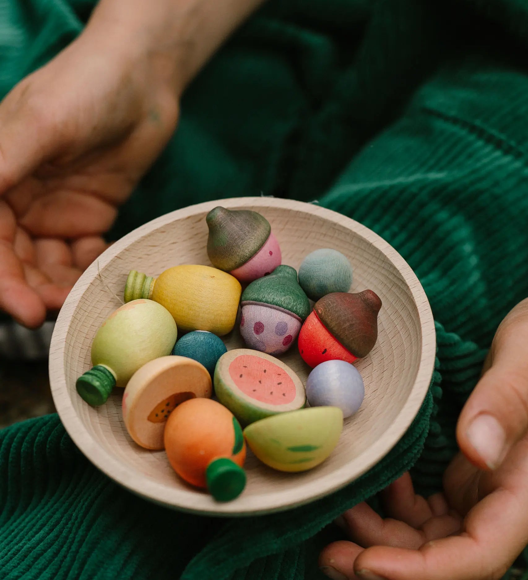 Close up Grapat's handcrafted wooden fruit pieces in a bowl on a child's knee showing hand painted detail