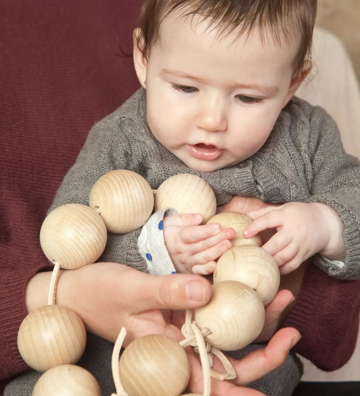 Baby holding the Grapat natural wooden sensory ball garland