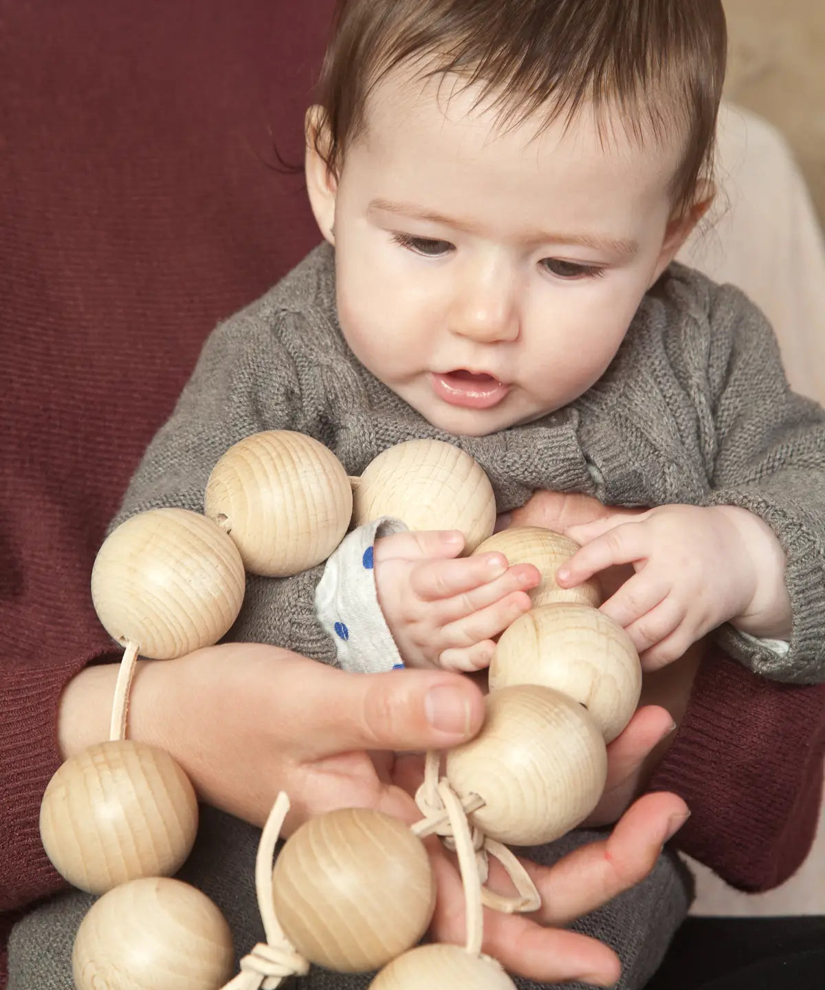 Baby holding the Grapat natural wooden sensory ball garland