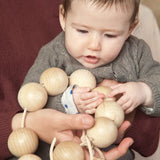 Baby holding the Grapat natural wooden sensory ball garland